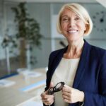 Woman standing in empty conference room holding glasses and smiling