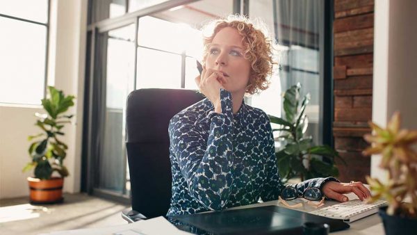 Business woman sitting in a well lit office looking into the distance thinking